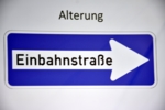 Zu sehen ist das Straßenverkejrsschild "Einbahnstraße" mit dem Schriftzug Alterung darüber.