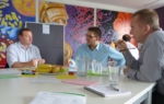 Zu sehen sind drei Fachleuten aus der IT und den Life Sciences, die in einem Besprechungsraum an einem runden Tisch sitzen und miteinander reden.