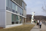 Zu sehen ist die Fensterfront eines modernen, dreistöckigen Gebäudes und eine Skulptur.