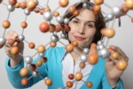 Zu sehen ist eine Frau, die das Modell eines Moleküls in der Hand hält.