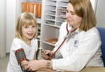 Zu sehen ist eine Ärztin im weißen Kittel, die einem Kind den Blutdruck misst.