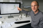Neher sitting in front of his computer, pointing at a drawing on the screen.