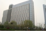 In the picture is a big grey building behind green trees.