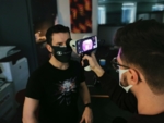 Ein Mann hält das Untersuchungsgerät in Richtung des Gesichts eines sitzenden Patienten, auf dem Smartphone das Foto des Augenhintergrunds.