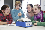 Auf dem Bild sind vier Schüler mit Schutzbrille beim Experimentieren zu sehen.