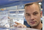 Coloured photo of Patrick Müller touching a shelf with a fish tank with zebrafish.