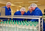 Drei Nycomed-Mitarbeiter und Wirtschaftsminister Ernst Pfister stehen an einem Tisch mit Glasflaschen und begutachten dahinter etwas für den Betrachter des Bildes nicht Sichtbares.