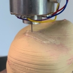 A skin-colored hemisphere printed with a silver needle in a 3D printer.