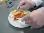 The photo shows two gloved hands that disect lasagne with tweezers and scalpel.