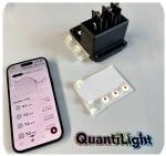 You can see a small black box with connectors protruding upwards, a transparent plastic cartridge and a mobile phone with an open app displaying the test results.