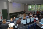 The photo shows people in an auditorium listening to a lecture.