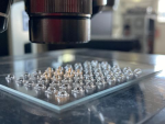 Rectangular glass plate with numerous convex, lens-shaped structures viewed under a microscope.