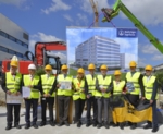 Zehn Personen, mit gelber Warnweste bekleidet und Helm auf dem Kopf, stehen auf einer Baustelle vor einem großen Banner von Boehringer Ingelheim, auf dem die Aufschrift "Wir bringen Innovationen" geschrieben steht.