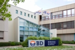 Gebäudefront mit Haupteingang, Firmenschild und Fahnen mit BD Logo
