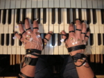 The photo shows hands playing on a piano. Infrared sensors are attached to the fingers.