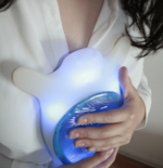Eine Frau, die sich das schildkrötenförmige weiß-blaue Gerät an die Brust drückt.