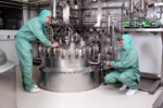 Ulm: Blick in biopharmazeutische Herstellung mit Edelstahl-Fermentern, zwei Mitarbeiter im Einsatz.