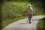 Eine ältere Dame läuft mit Walking-Stöcken über einen Weg. Man sieht die Dame von hinten.