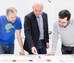 Foto von einem Wissenschaftlerteam, das an einem Schreibtisch steht und ein Experiment plant.