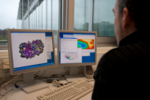 Ein Forscher sitzt vor zwei Bildschirmen und visualisiert ein Protein am Bildschirm, indem er eine Software zum Design verwendet.