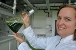 Prof. Heike Frühwirth holding an Erlenmeyer flask filled with green liquid. The green colour is due to the algae contained in the liquid.