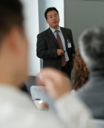 An Asian in a dark suit presenting data.