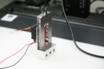 The photo shows a small metal device with wires and standing in a mount.