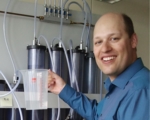 Prof. Dr. Alexander Wittemann in seinem Labor stehend mit einem Messbecher in der Hand.