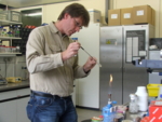 Dr. Christoph Mayer im Mikrobiologielabor der Uni Konstanz mit Reagenzglas in der Hand vor einem Gasbrenner.