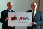 Wissenschaftsminister Frankenberg und Gründungspräsident Wolff präsentieren das neue Logo der Dualen Hochschule Baden-Württemberg. Das Logo trägt die Schriftzüge "DHBW", darunter "Duale Hochschule Baden-Württemberg".