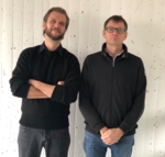 Two men standing in front of a white wall