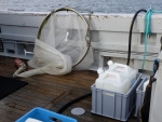 Ship deck on the sea showing a fishing net and two canisters with liquid.