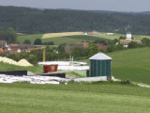 Das Bild zeigt eine Biogasanlage und im Hintergrund ein Dorf.