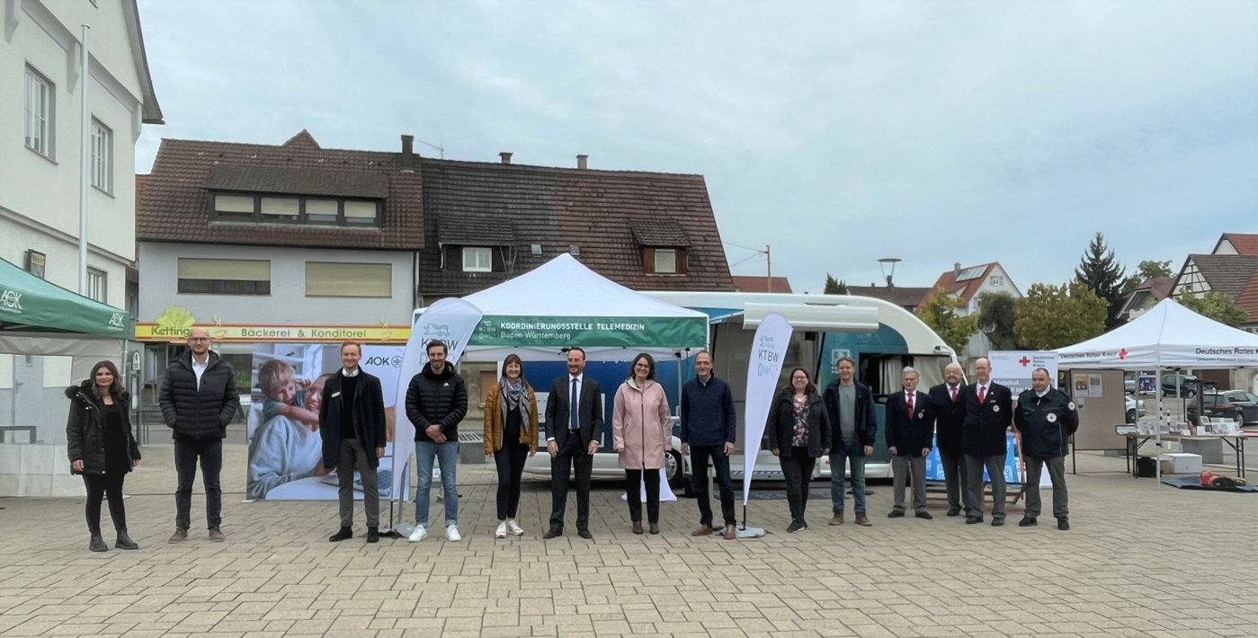 Eine Gruppe von Menschen steht in einer Reihe vor dem Pavillon der Koordinierungsstelle Telemedizin Baden-Württemberg und dem Digitale Health Truck. Links sieht man ein Banner der AOK und rechts den Stand des Deutschen Roten Kreuzes.